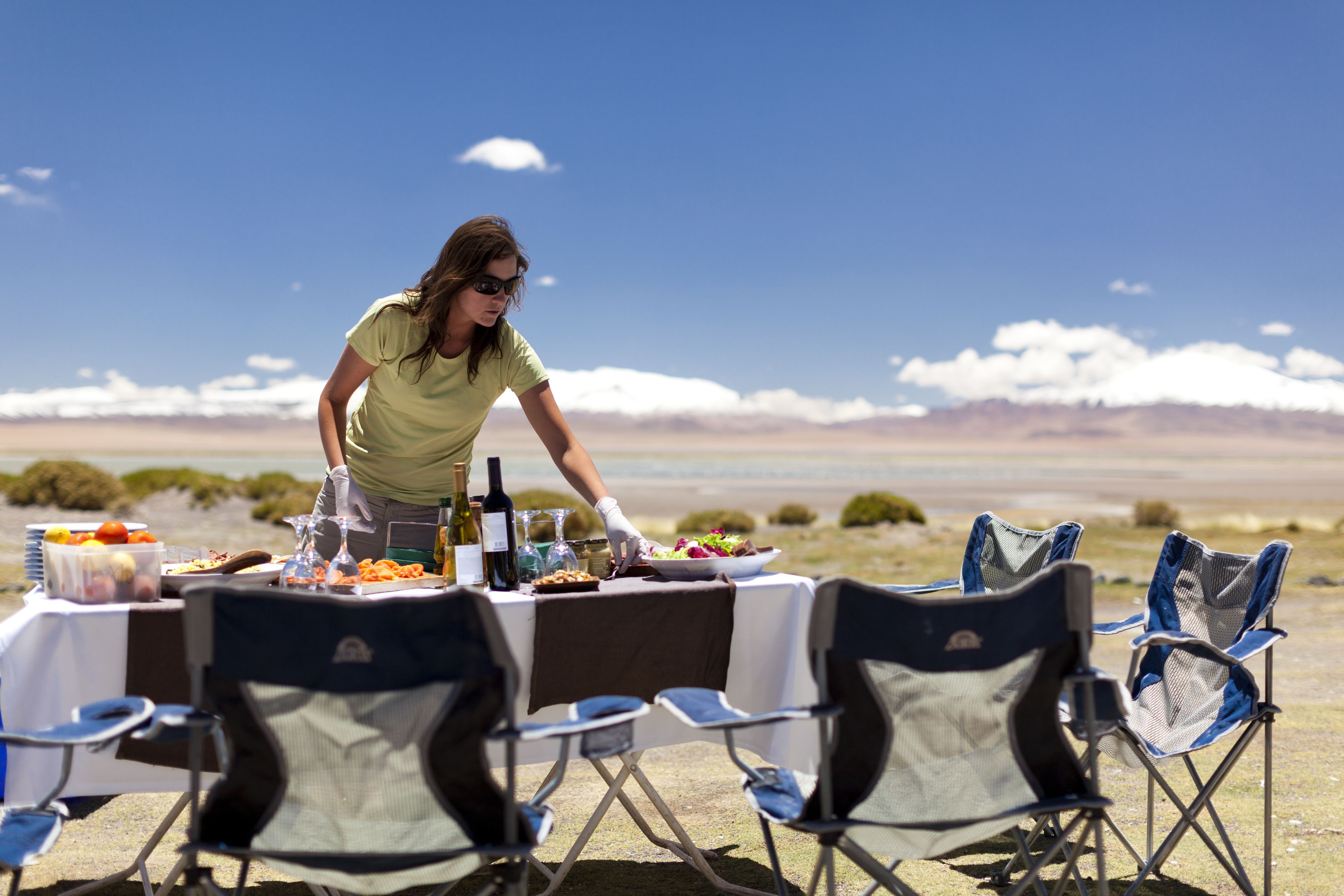 Una mesa con sillas dispuesta para comer, y una persona sirviendo comida.