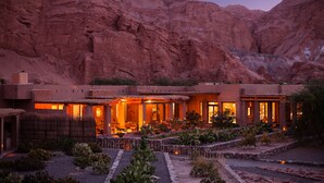 Un resort en el desierto con un amplio patio, varias habitaciones con grandes ventanales y vistas a formaciones rocosas rojas.
