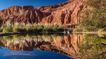 A serene landscape with a clear reflection in a calm body of water, surrounded by red rock formations and sparse vegetation.