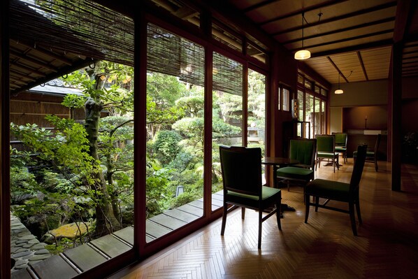Una habitación tradicional japonesa con suelo de tatami, vistas a un jardín exuberante a través de amplias puertas correderas y techo de madera.