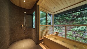 Un baño moderno con una bañera de madera, ducha y un amplio ventanal con vistas al bosque.