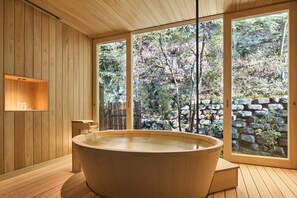 Interior de madera con una bañera grande, paredes de madera y vista a un jardín rocoso a través de amplias ventanas.