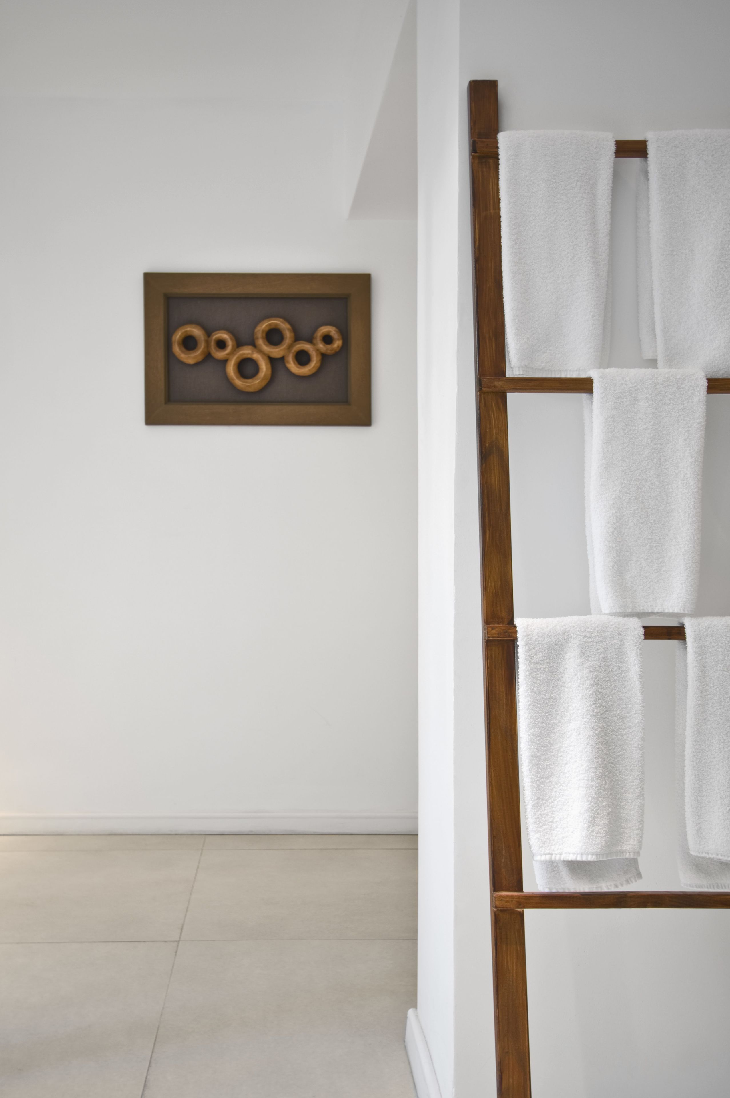 A bathroom with a wooden towel rack holding several white towels, a framed picture on the wall, and a tiled floor.