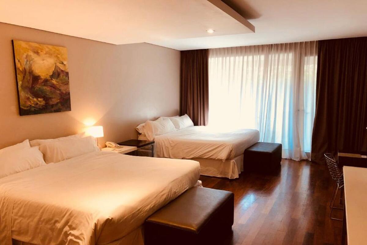 A hotel room with two beds, a desk, a chair, and a painting on the wall.