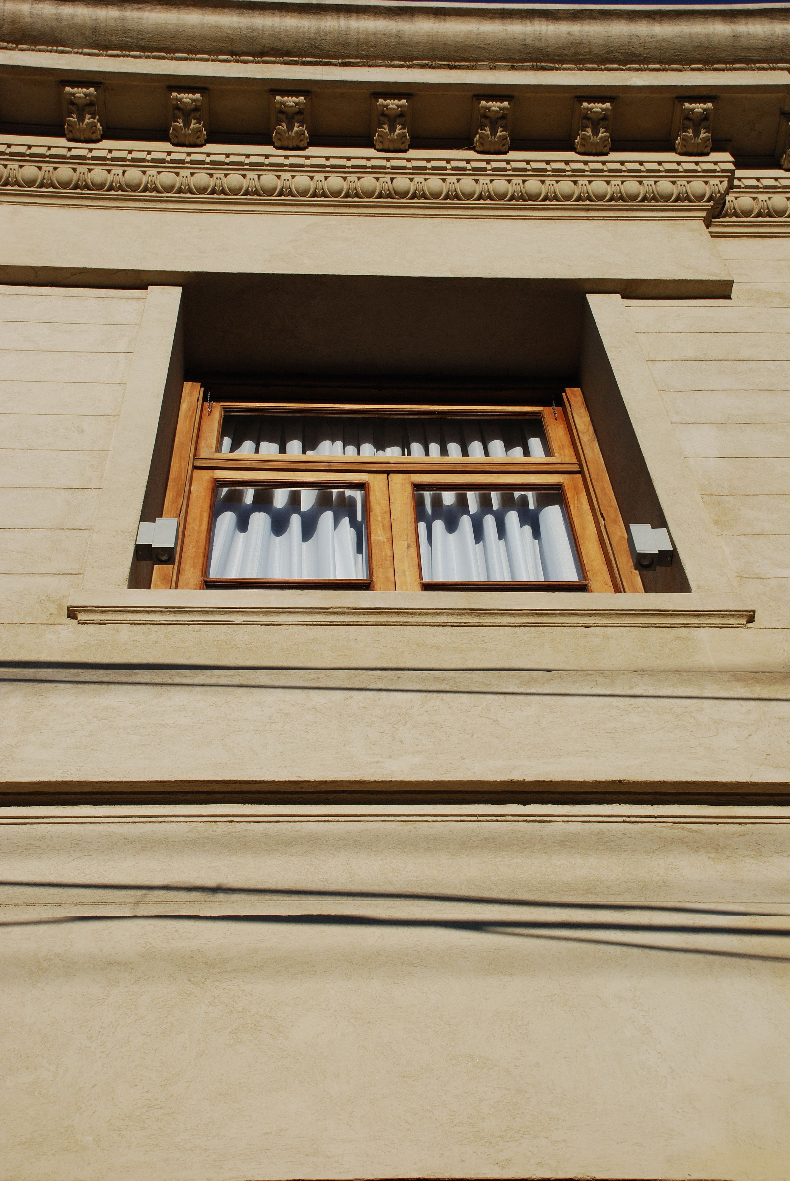 A building facade with a window featuring a wooden frame and white curtains.