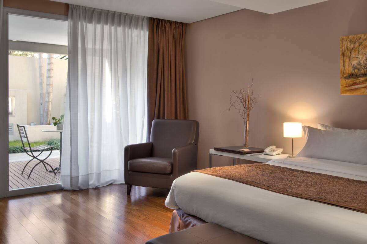 A hotel room with a bed, a chair, a table with a lamp, and a phone.