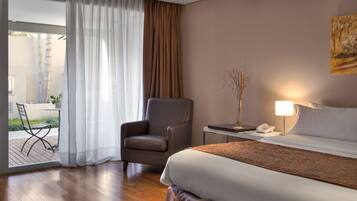 Quarto de hotel com uma cama, uma cadeira, uma mesa com abajur e um telefone.