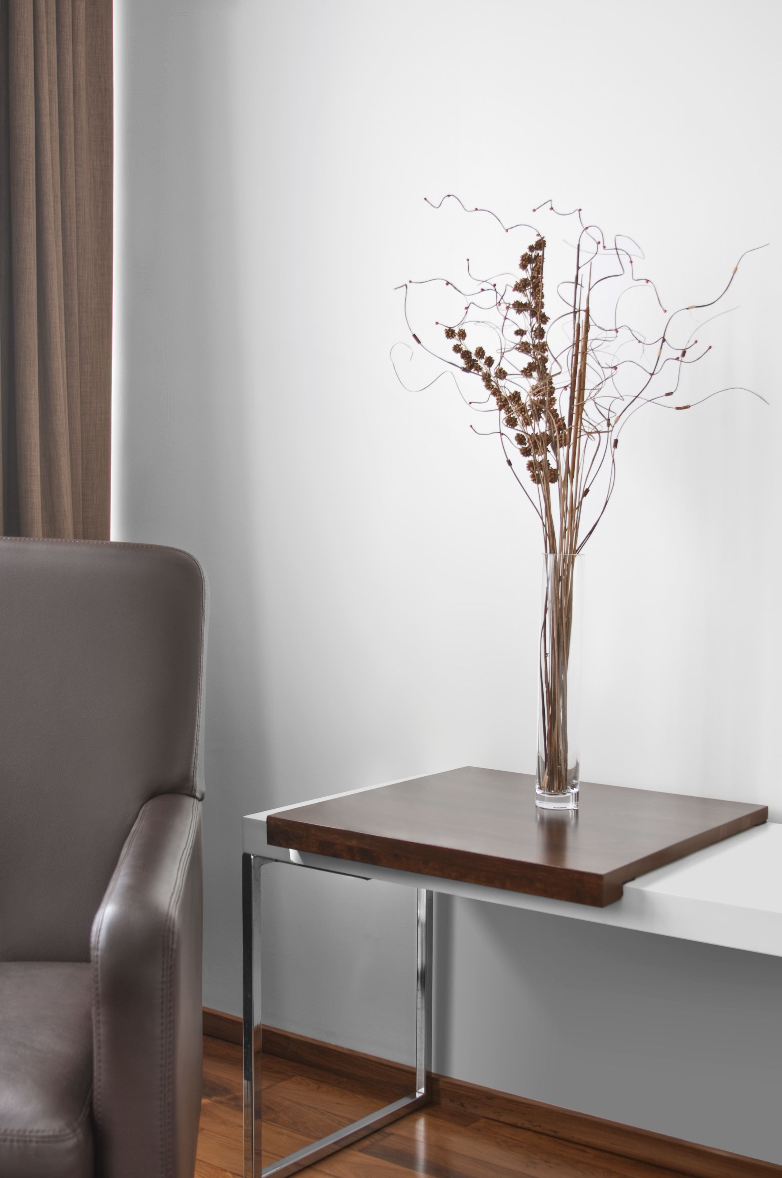 Una habitación moderna con un sillón de cuero, una mesa de madera y un jarrón con plantas secas.