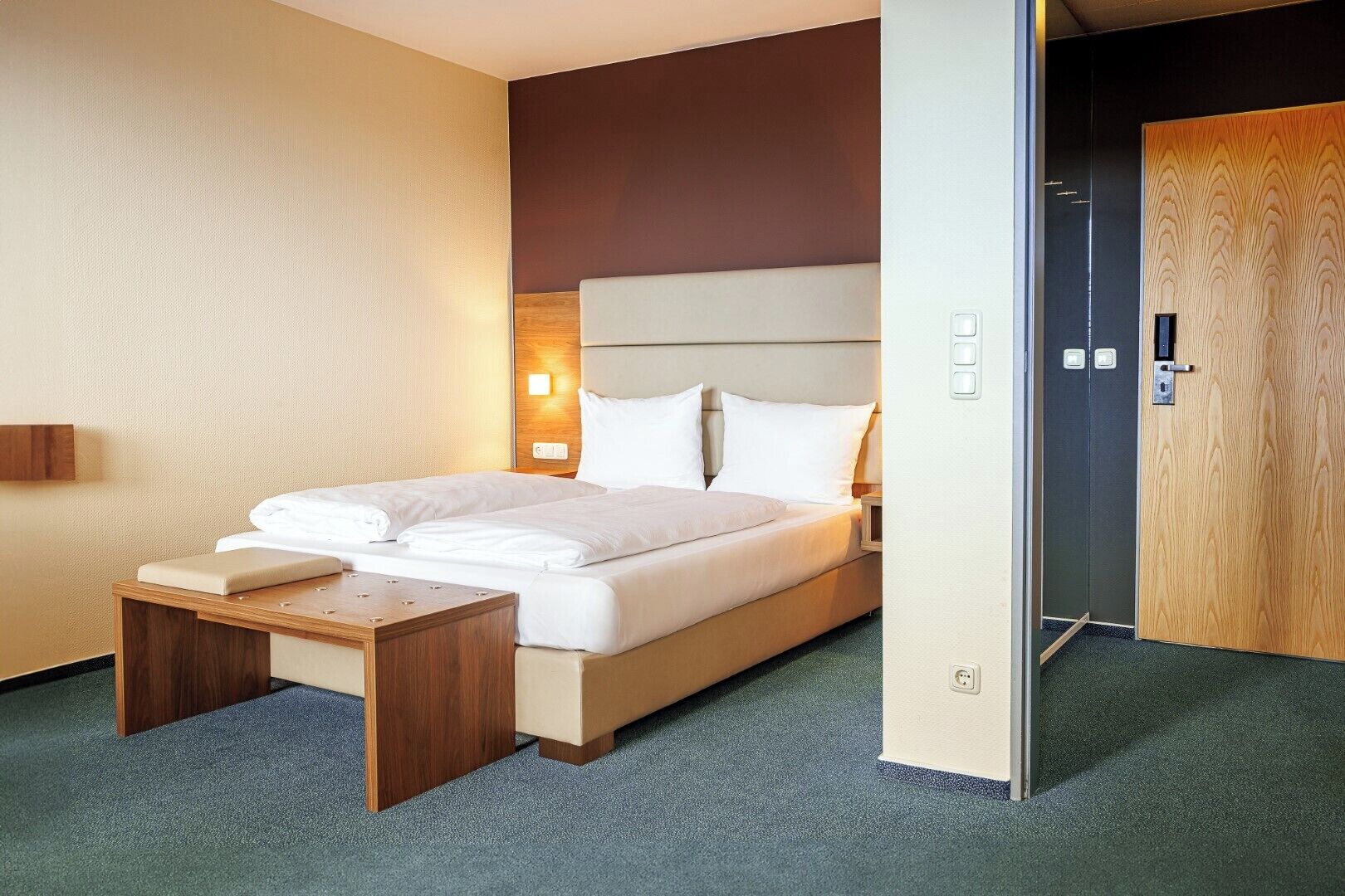A hotel room with a bed, bedside table, and a wooden door.