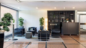 A modern lobby with leather seating, a reception desk, and a display of bottles and glasses. - GenoHotel Forsbach (Roesrath)