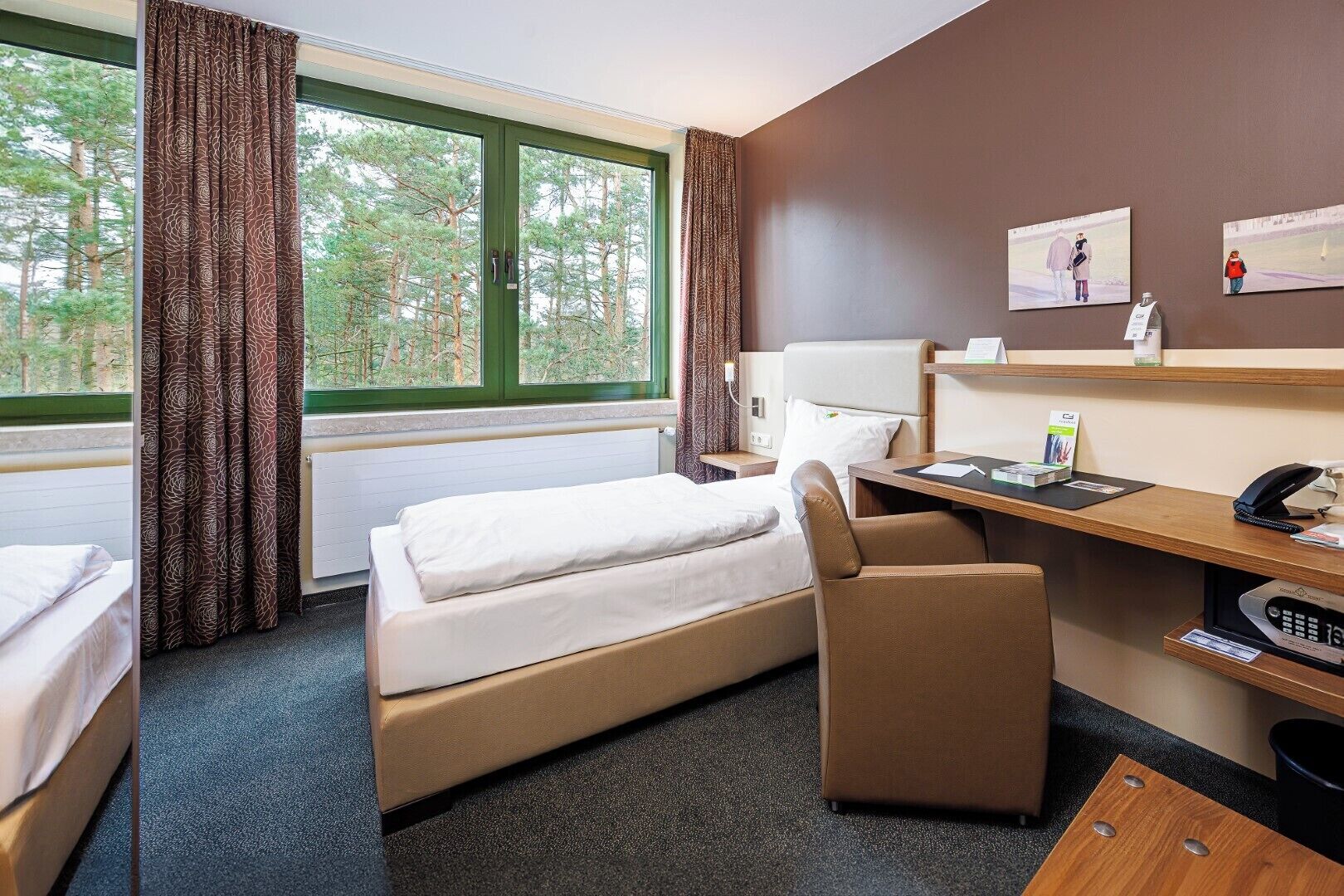 Hotellihuone, jossa on sänky, työpöytä, tuoli ja ikkunasta avautuva näkymä puistoon.