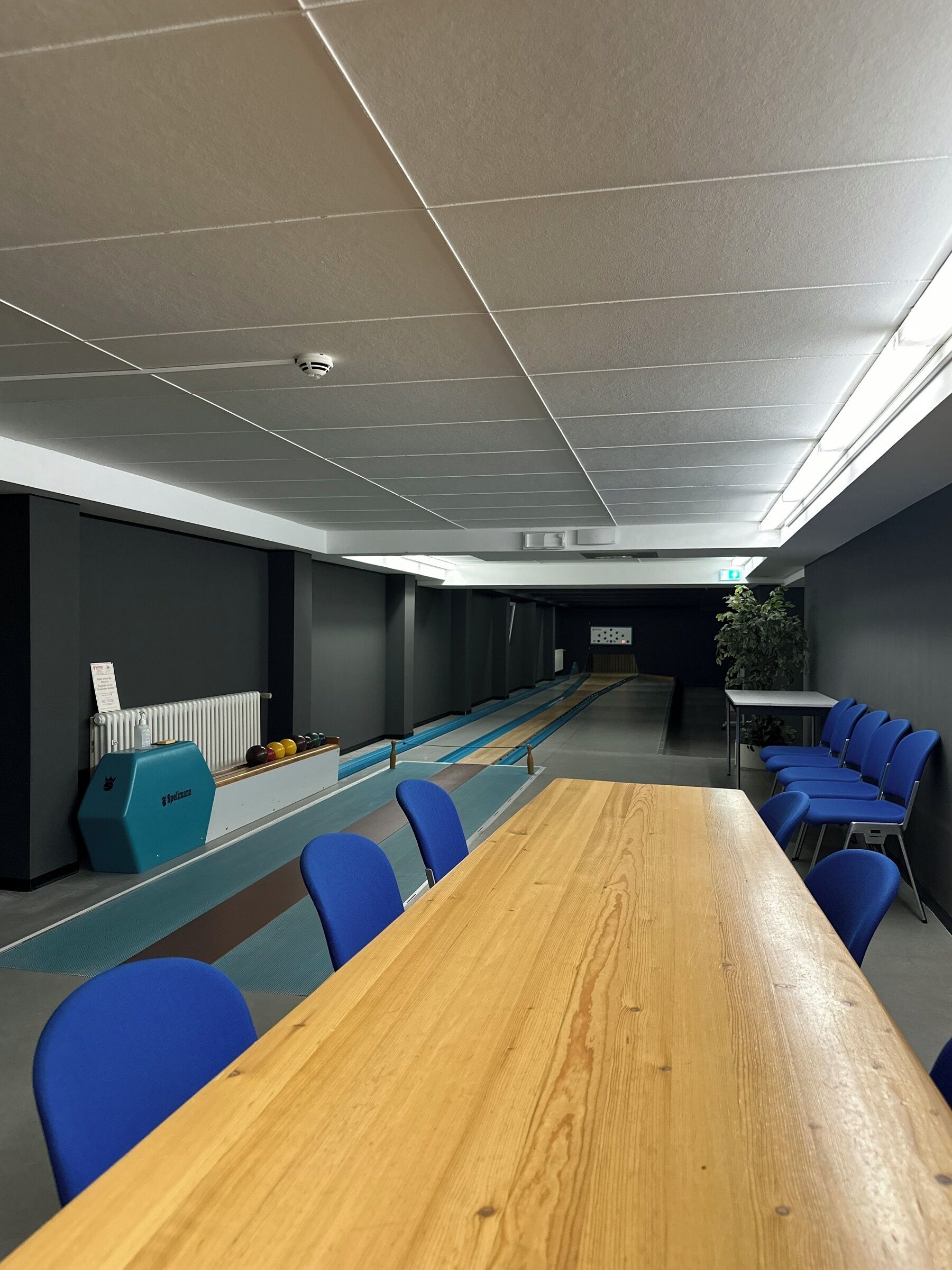 Ein Konferenzraum mit einem langen Holztisch und blauen Stühlen, einem Heizkörper und einem blauen Schrank mit einem Logo.
