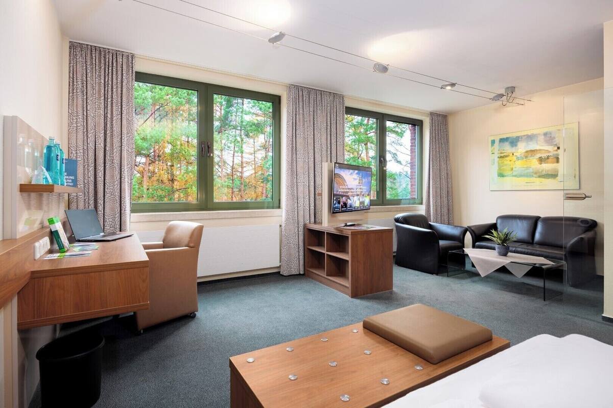 Habitación de hotel con escritorio, dos sillas, sofá, televisión y un cuadro en la pared.