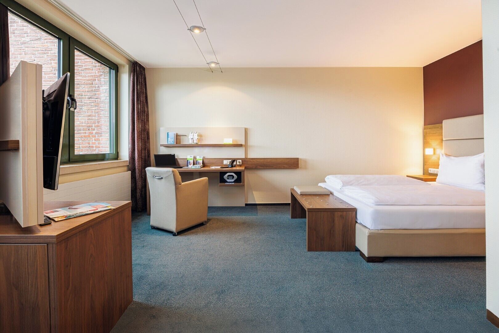A hotel room with a bed, a desk, a chair, a TV, and a window with curtains.