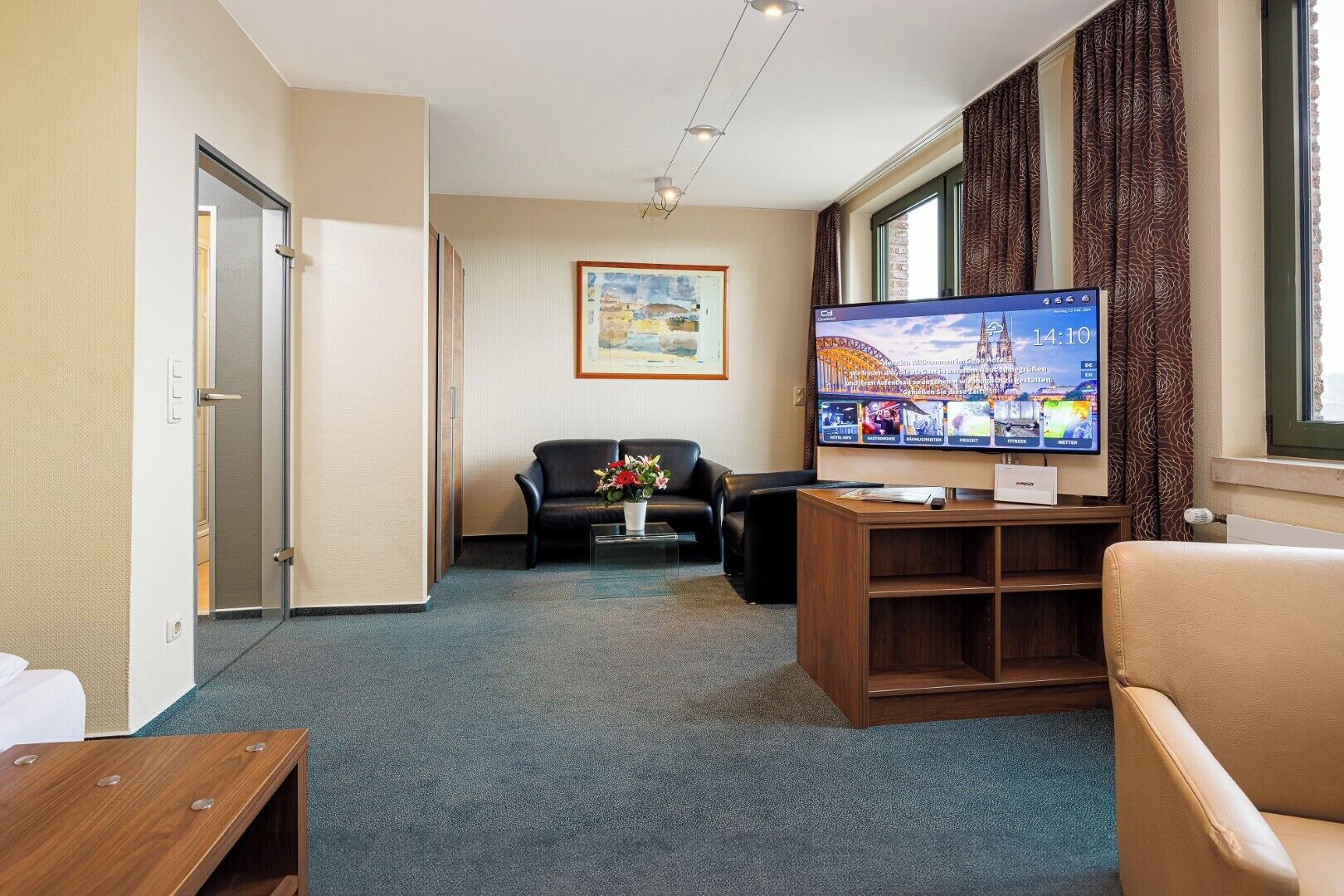 A hotel room with a TV, a sofa, a coffee table, and a window with curtains.