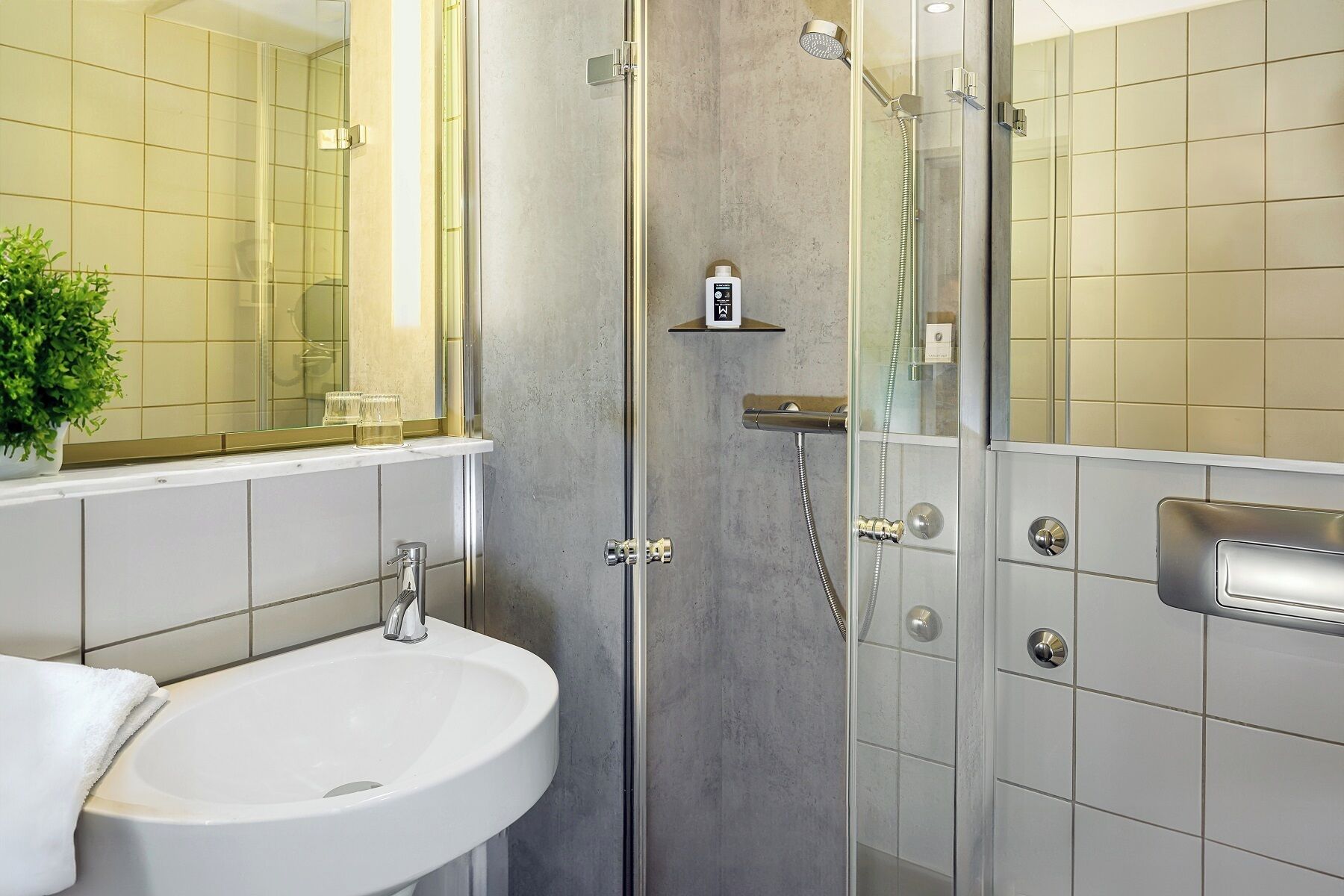 A modern bathroom with a glass-enclosed shower, a white sink, and a small shelf with toiletries.