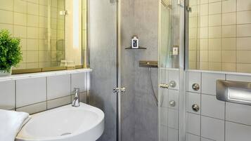A modern bathroom with a glass-enclosed shower, a white sink, and a small shelf with toiletries.