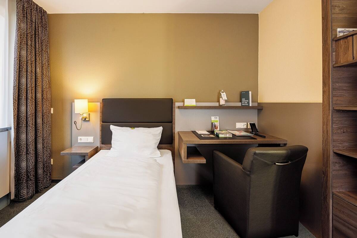 Una habitación de hotel con cama, escritorio, silla, mesita de noche y estante con amenidades.