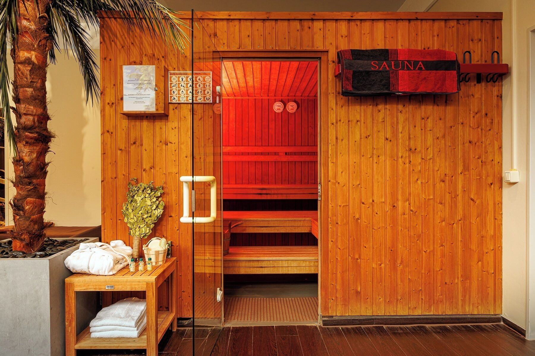 A sauna room with wooden walls and benches, a towel rack, and a sign reading "SAUNA".