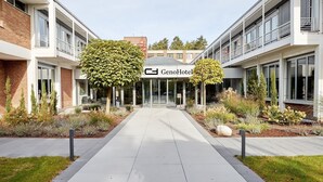 A modern hotel entrance with a clear pathway, glass doors, and a sign reading "GenoHotel". - GenoHotel Forsbach (Roesrath)