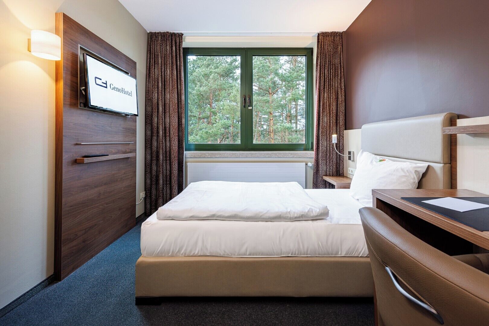 A hotel room with a bed, a desk, a TV, and a window with curtains.