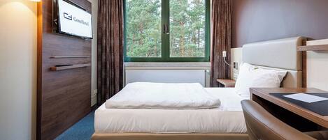 A hotel room with a bed, a desk, a TV, and a window with curtains.