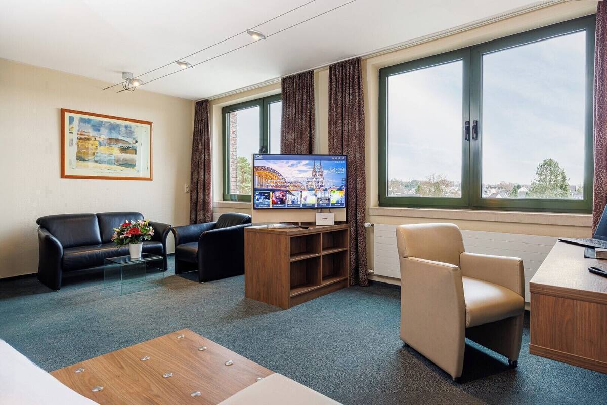 Habitación de hotel con televisión, sofá, silla, escritorio y ventana grande.