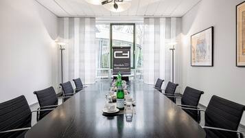 A conference room with a long table, black chairs, and a large window with curtains.