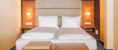 A neatly made bed with white linens, two bedside tables with lamps, and a wooden bench at the foot of the bed.
