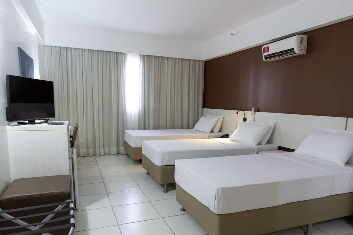 Una habitación de hotel con dos camas individuales, un televisor, un escritorio y un aire acondicionado.