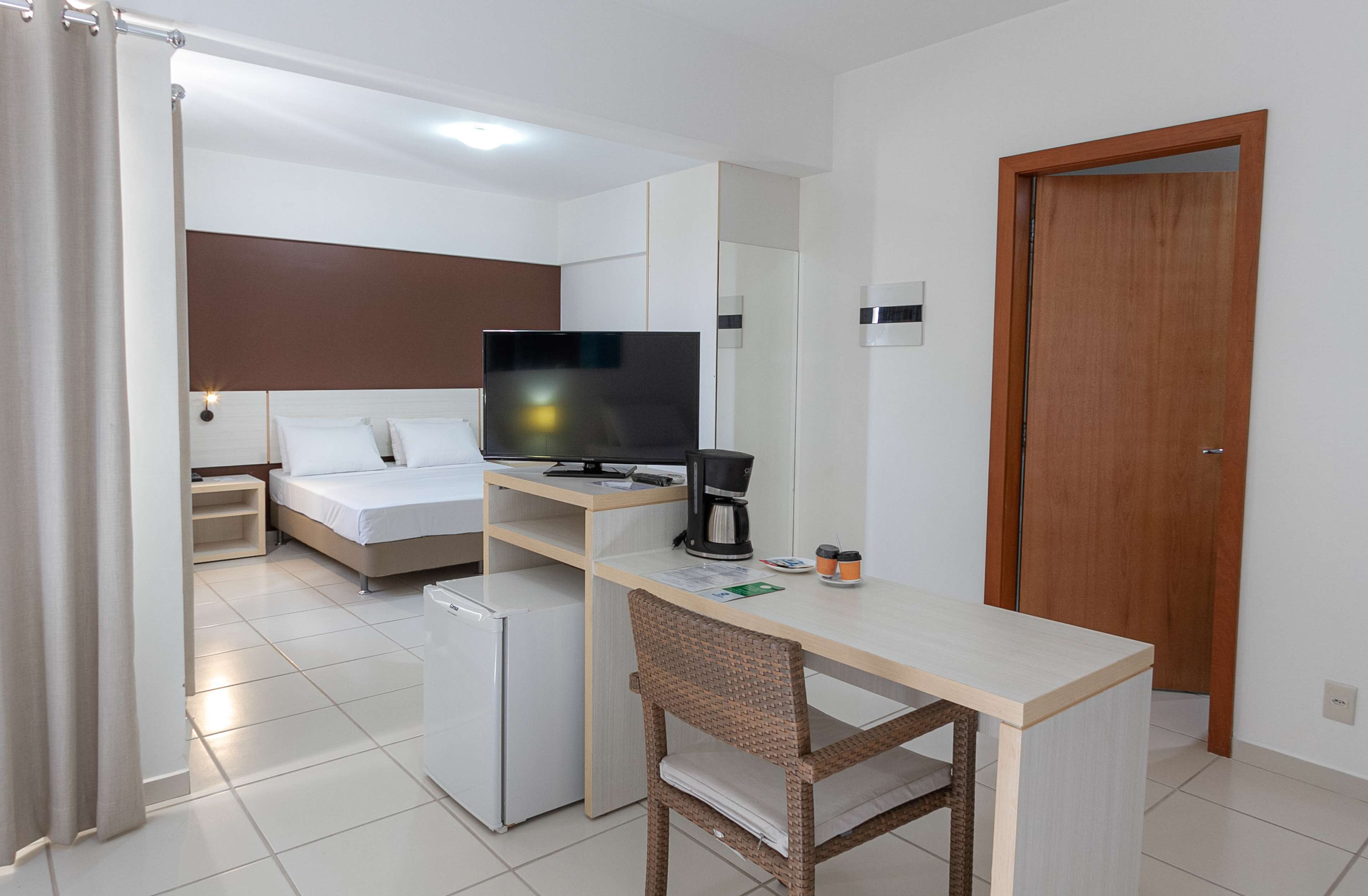 Ein kompaktes Hotelzimmer mit einem Bett, einem Schreibtisch mit Fernseher, einer Kaffeemaschine und einem kleinen Kühlschrank.