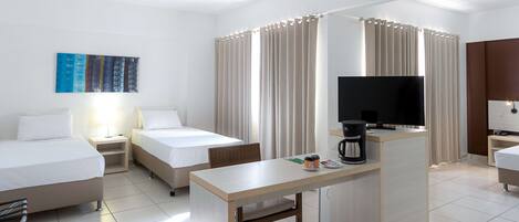 Una habitación de hotel con dos camas, un escritorio con cafetera, televisión y cortinas.