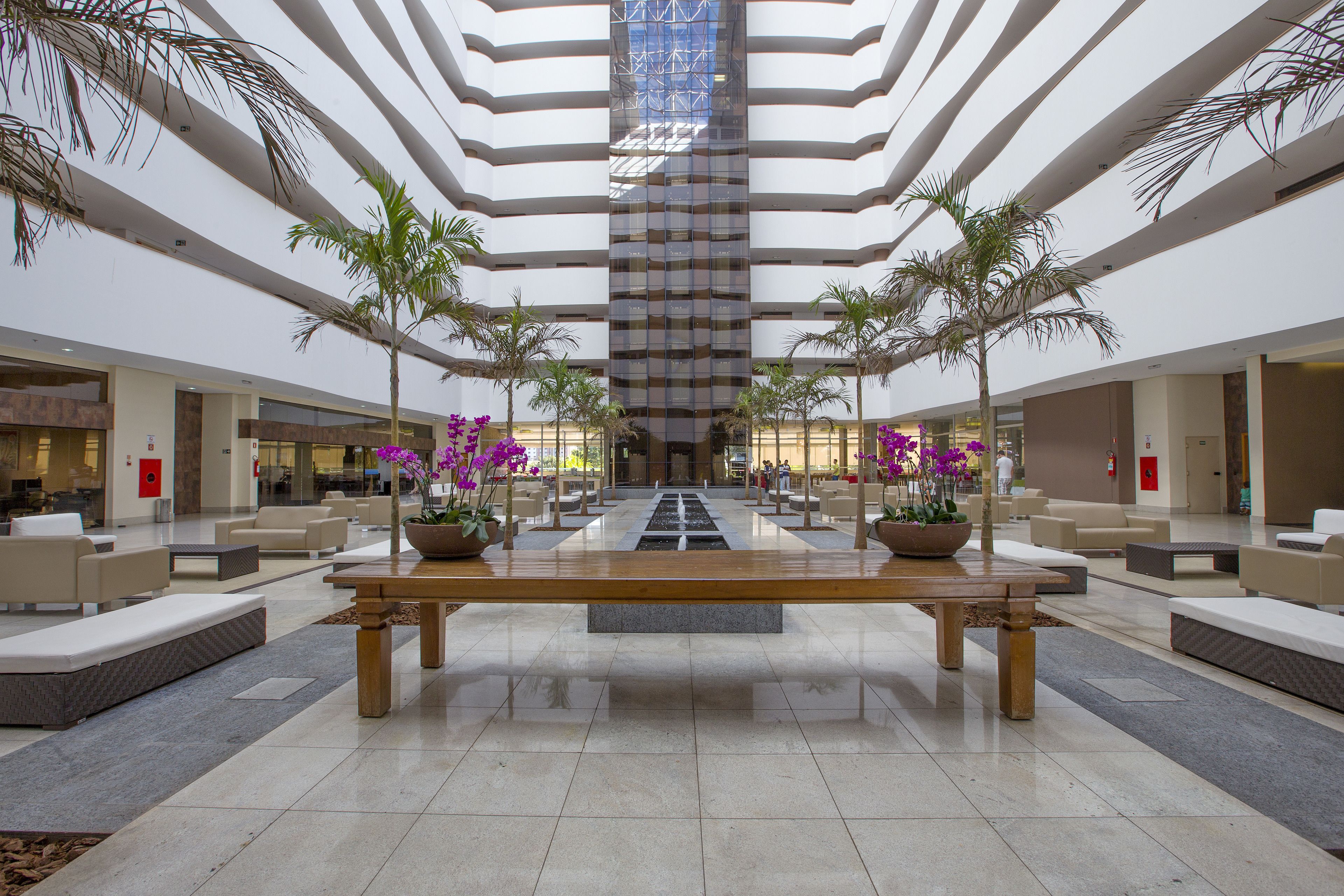 A spacious lobby with a central water feature, multiple seating areas, and potted plants.