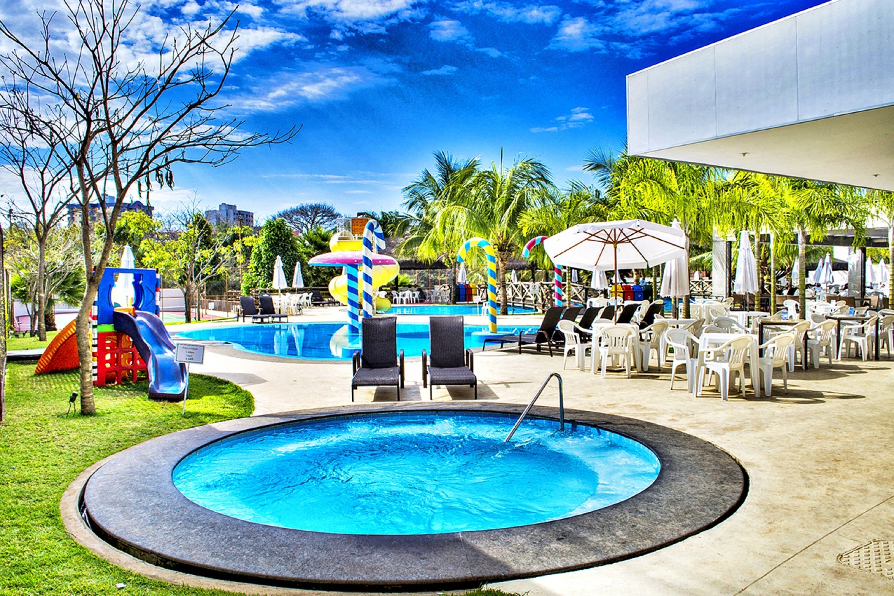 A pool area with a circular pool, lounge chairs, umbrellas, and a slide.
