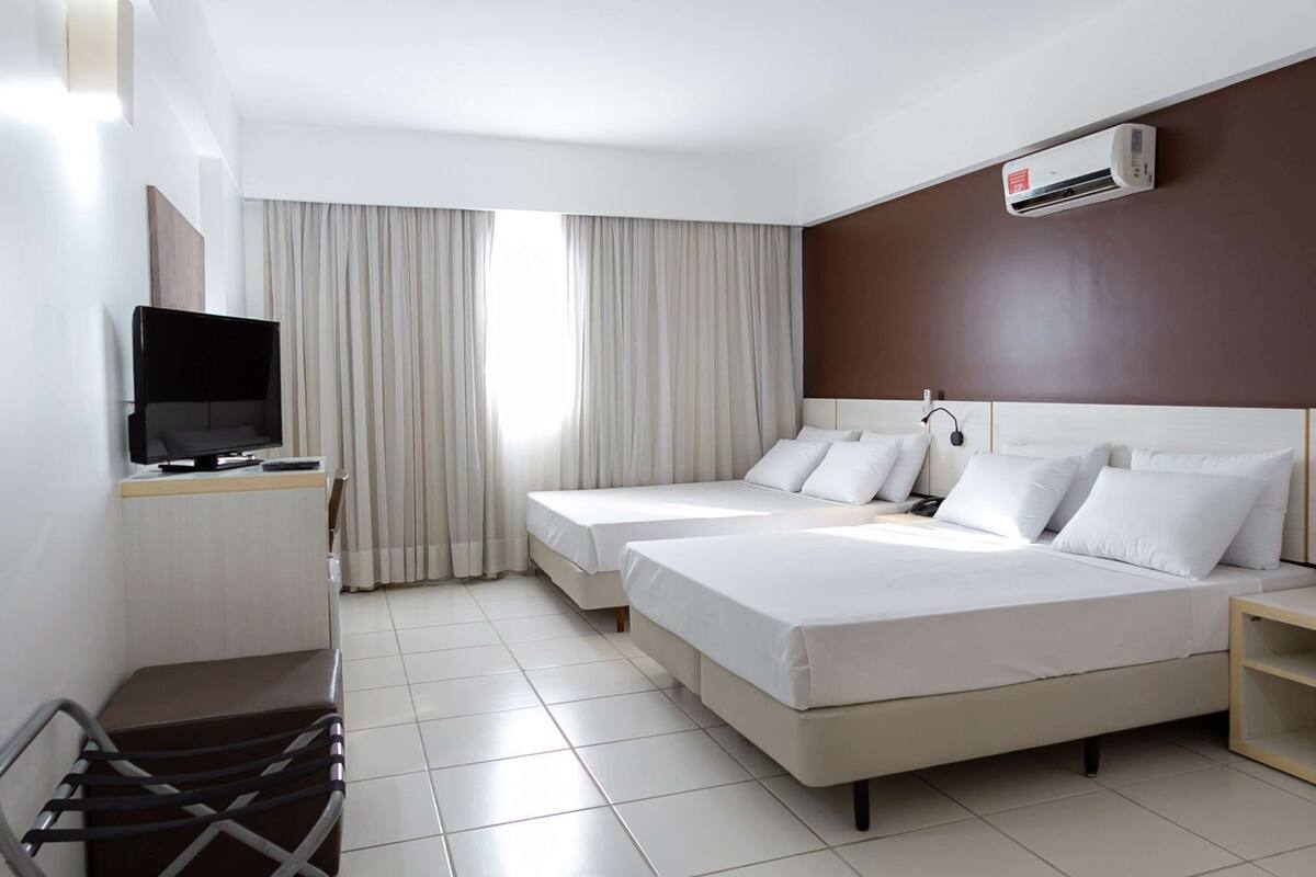 Habitación de hotel con dos camas, televisión, escritorio y aire acondicionado.