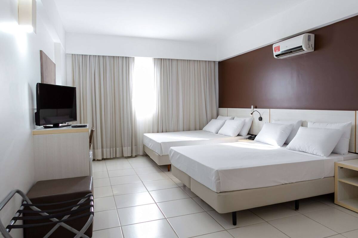 Una habitación de hotel con dos camas, un televisor y aire acondicionado.