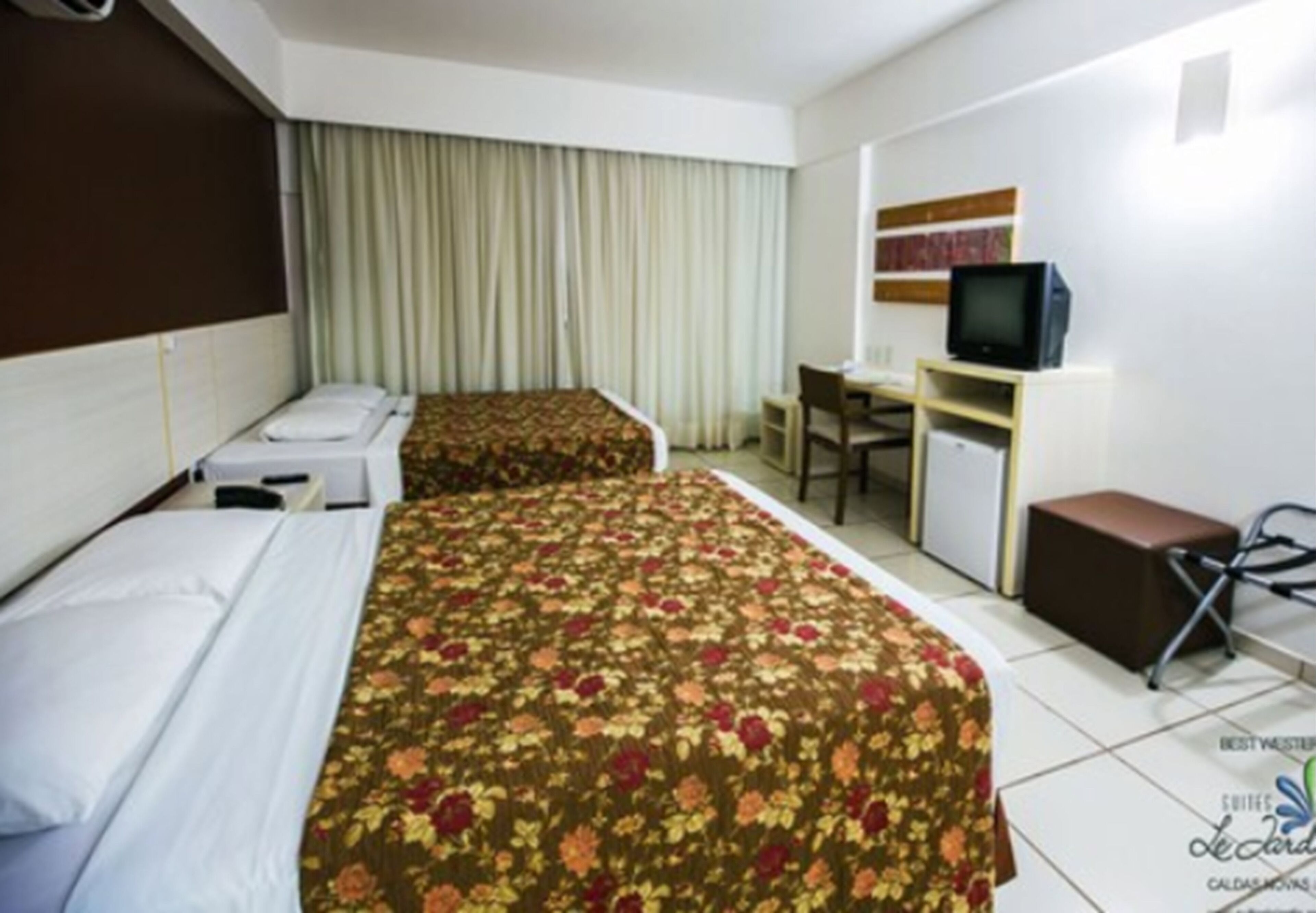 Une chambre d’hôtel avec deux lits, un bureau, une télévision et un petit coin salon.