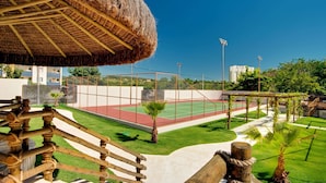 Una cancha de tenis con una red, rodeada por una cerca y una estructura de techo de paja.