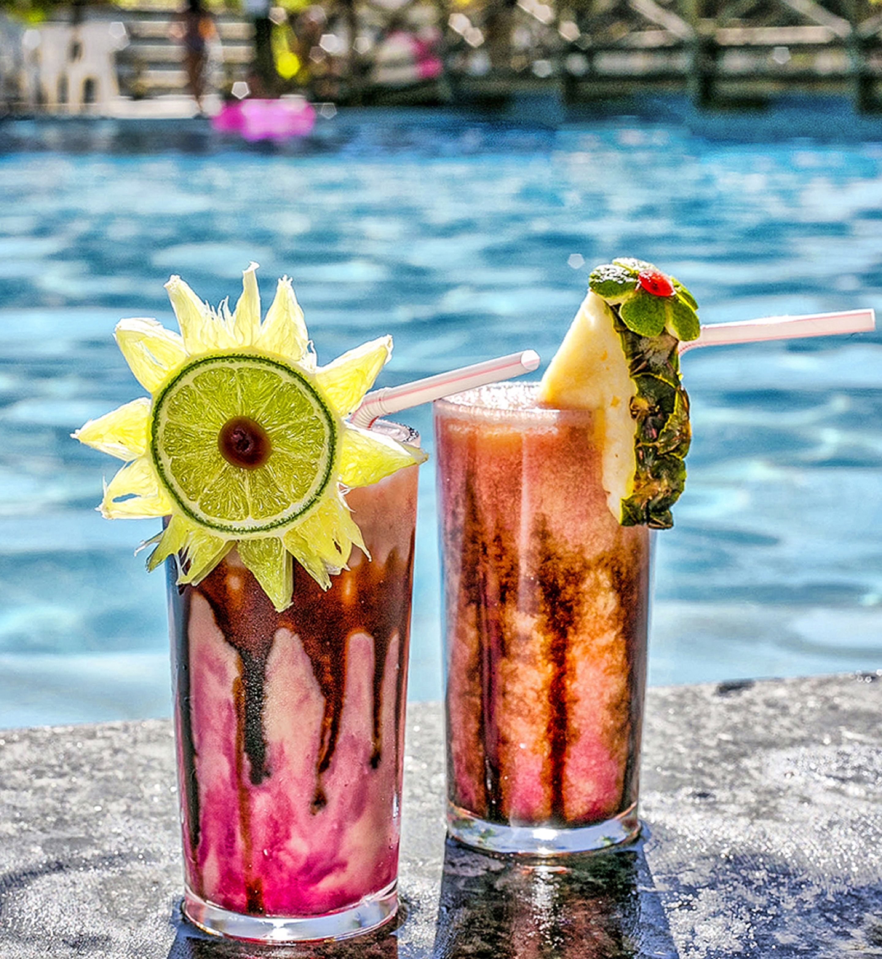 Two cocktails with garnishes, a pool in the background.