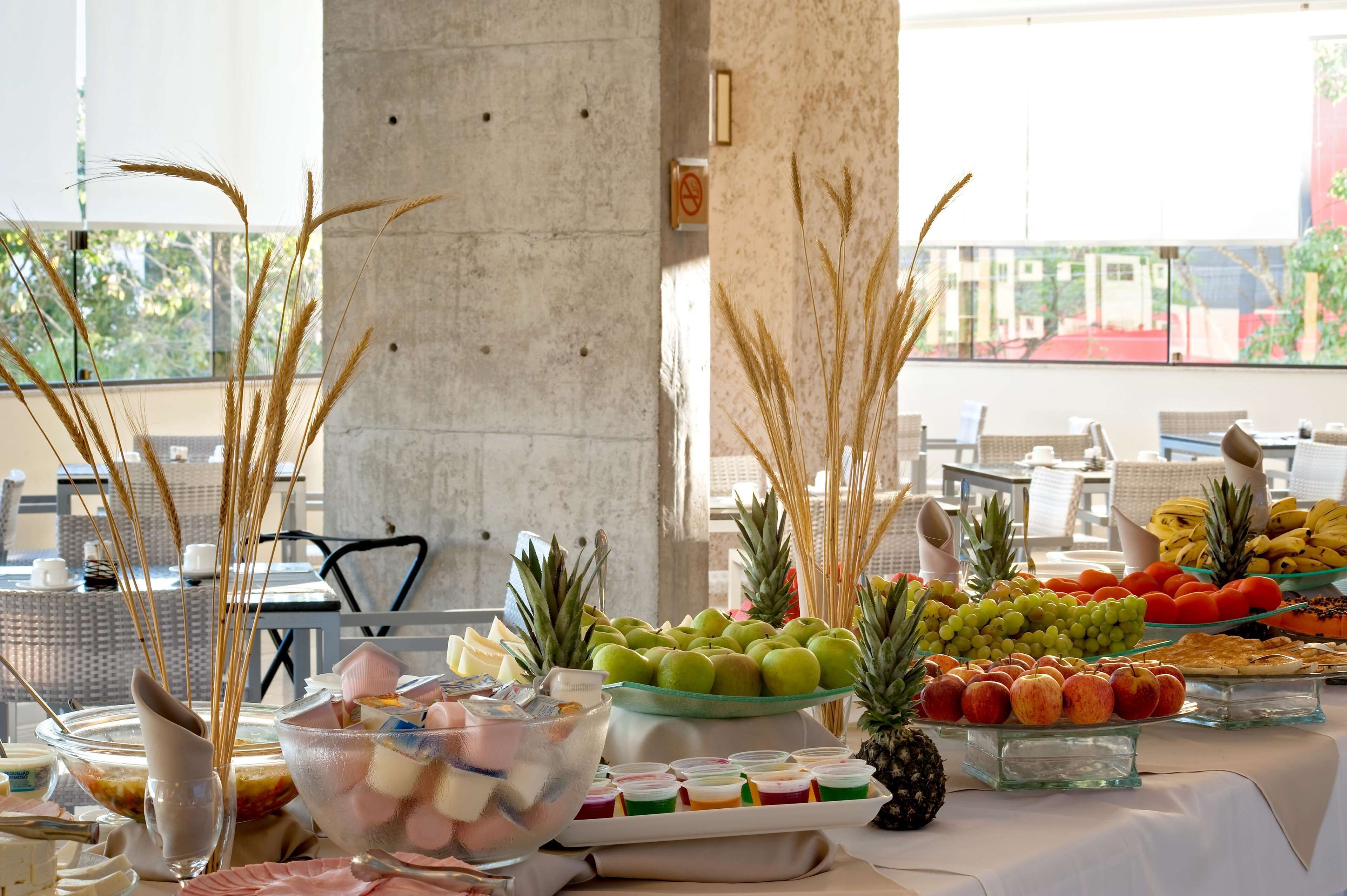 A buffet table with various fruits and desserts, a view of the outdoors, and a concrete pillar in the background.