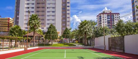 A tennis court with a net, surrounded by palm trees and buildings.