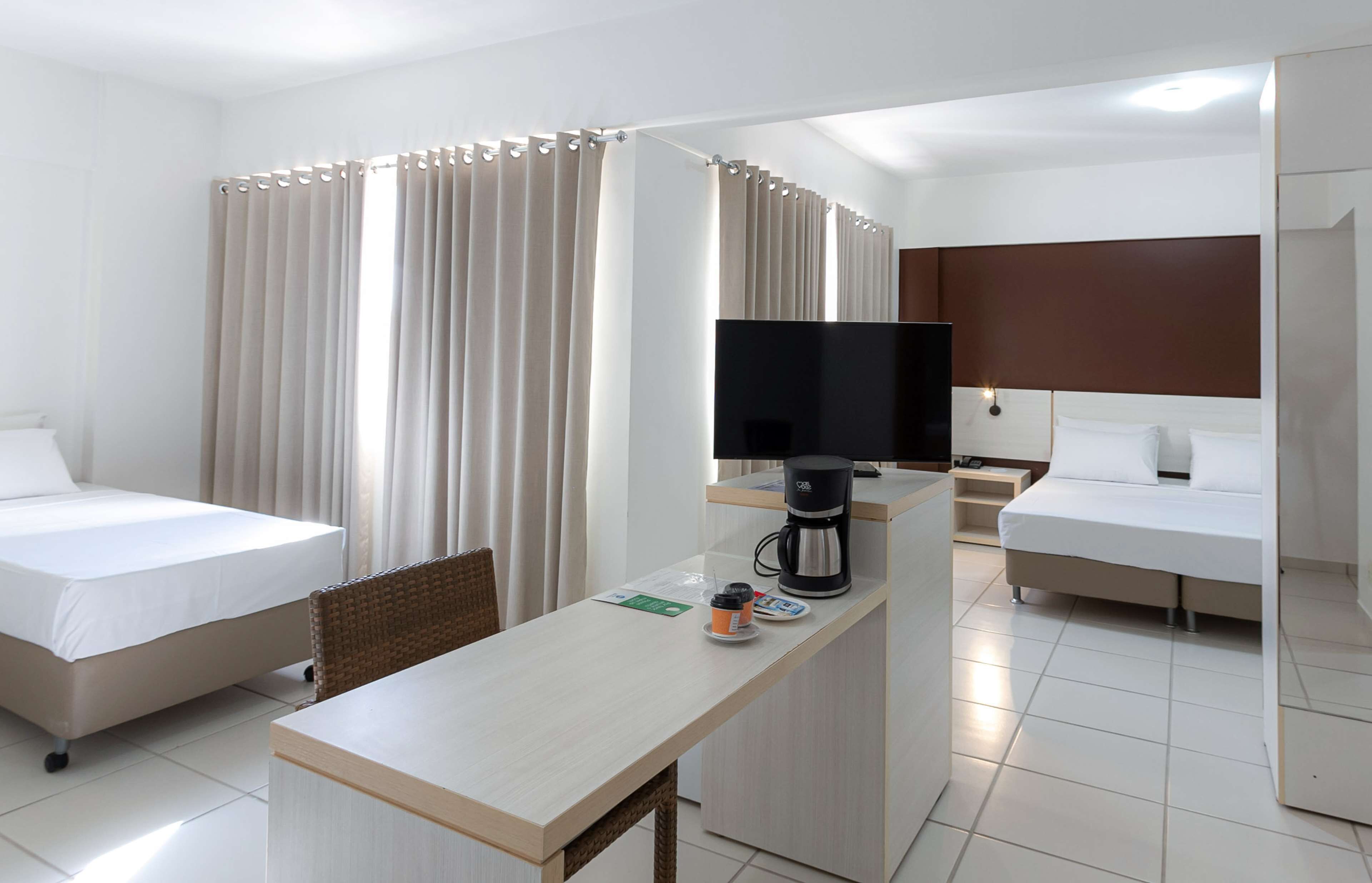 Ein Hotelzimmer mit zwei Betten, einem Schreibtisch mit Kaffeemaschine und einem Fernseher.