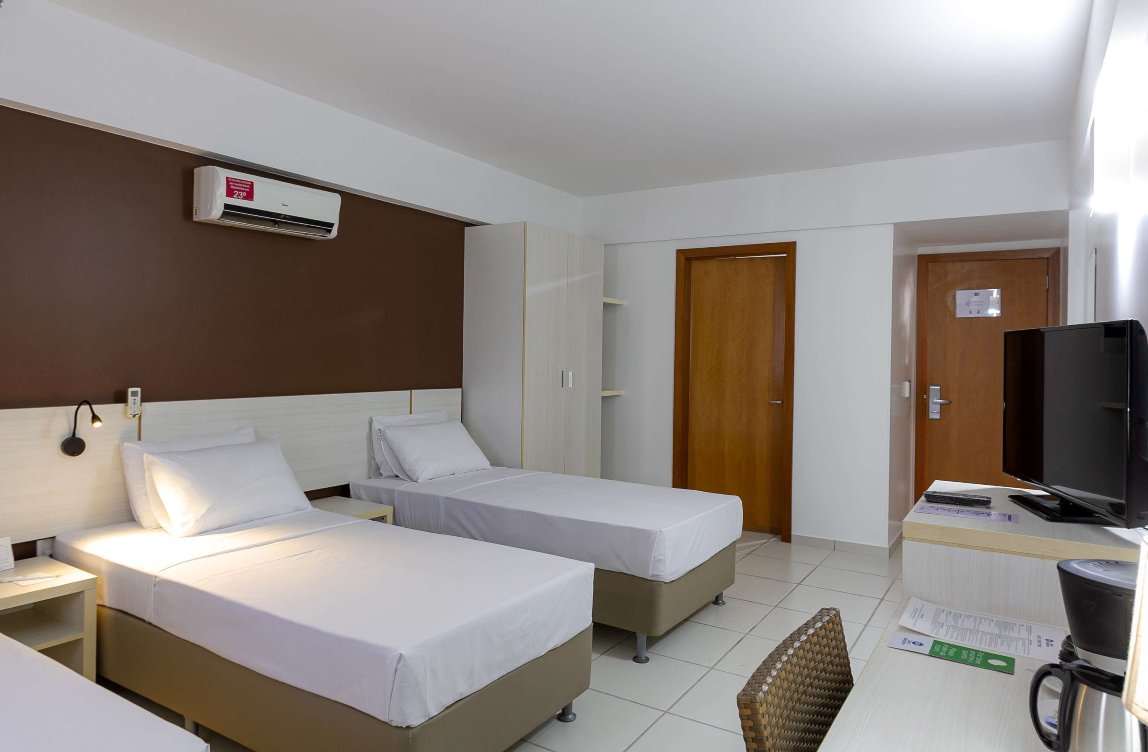A hotel room with two single beds, a TV, a coffee machine, and a wooden door.