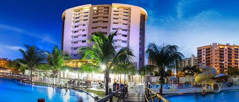 A resort with a large pool, a wooden bridge, and a tall building with multiple balconies.