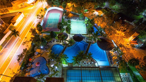 Vista aérea de un resort con múltiples canchas de tenis, una zona de piscina y palmeras circundantes.