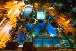 Vista aérea de un resort con múltiples canchas de tenis, una zona de piscina y palmeras circundantes.