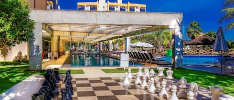A poolside area with a checkered chessboard, lounge chairs, and a building with a modern design.