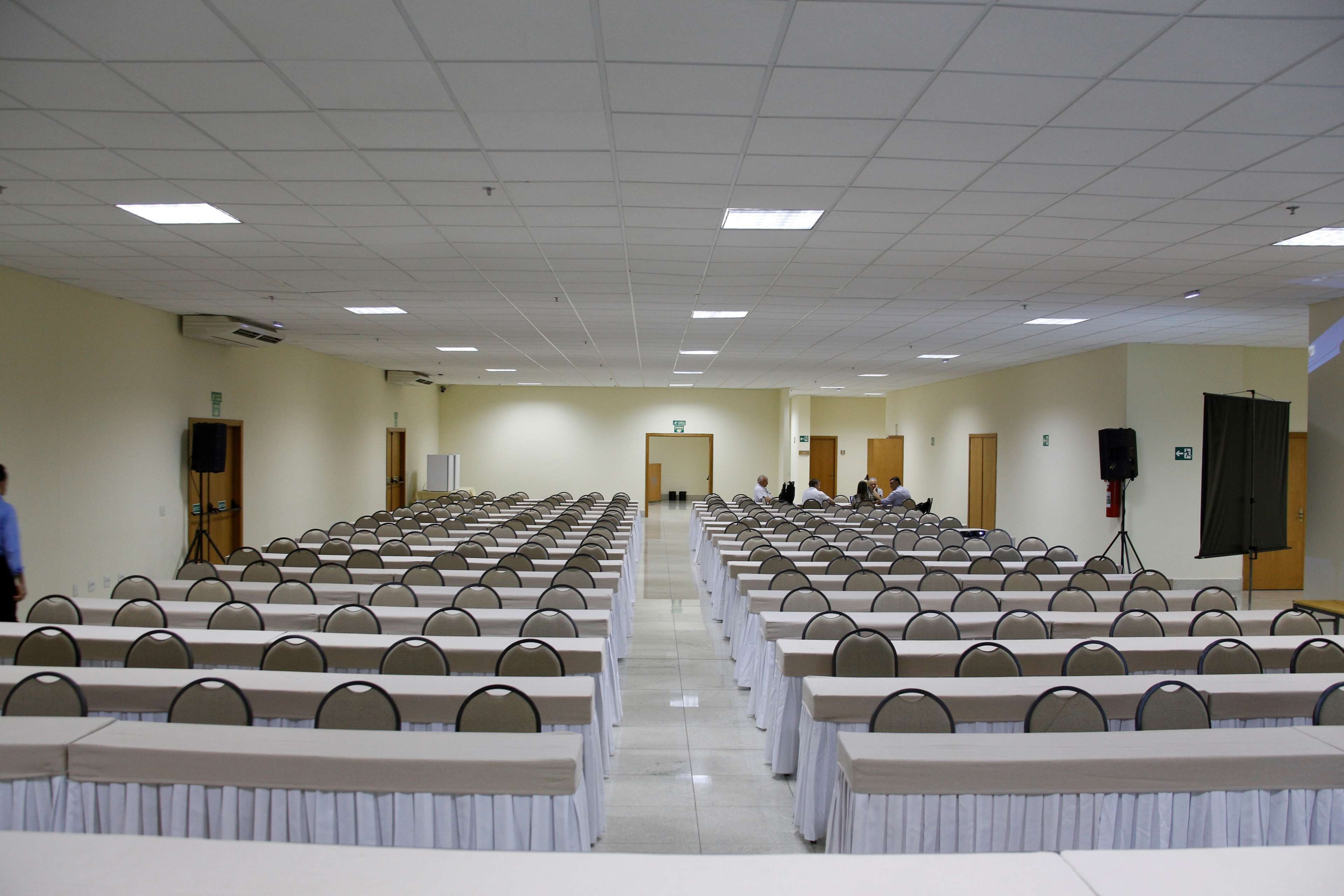 A conference room with rows of tables and chairs, a stage at the front, and a projector screen.