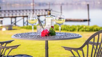 A round metal table with three glasses of white wine, a bottle, and a red flower centerpiece.
