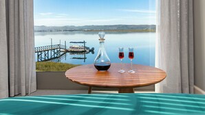 A room with a view of a lake, a wooden table with a decanter and two glasses of red wine, and a bed with a teal bedspread. - St James of Knysna (Knysna)